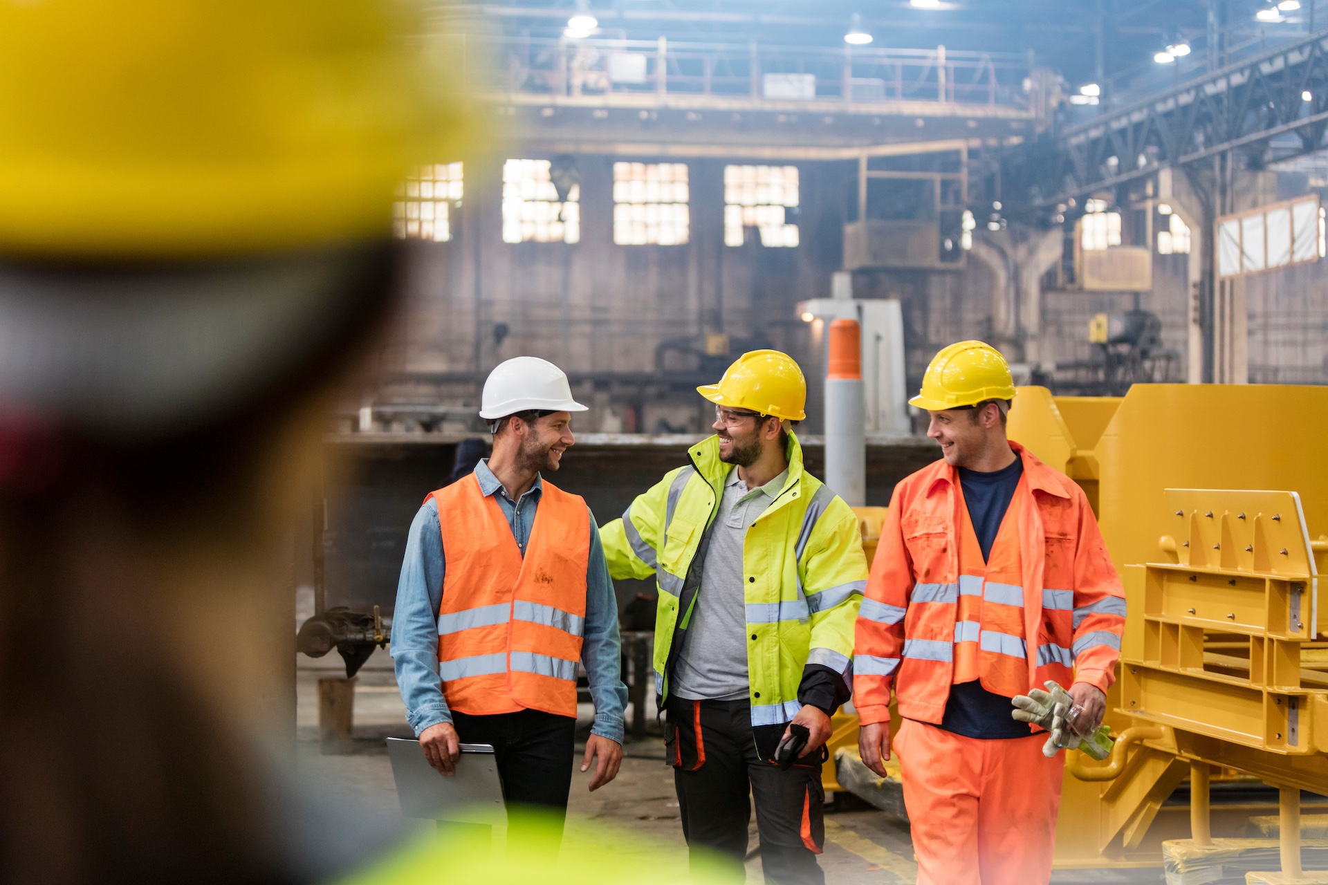 Construction workers in safety gear discussing at industrial site.